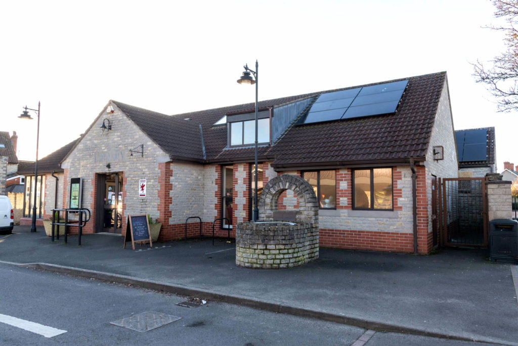 Exterior of Somerton Library, a modern stone and brick building with solar panels on the roof, accessible entrance and a historic stone well feature outside.