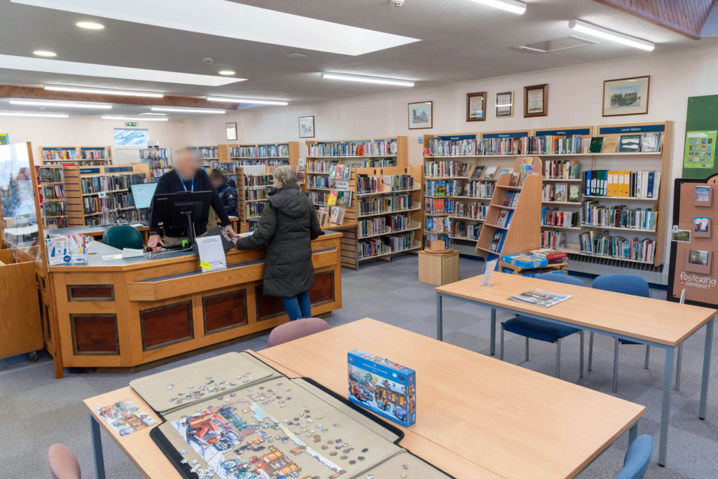 Main library area at Somerton Library with customer service desk, biography and local history collections, community tables and a shared jigsaw puzzle activity for visitors.