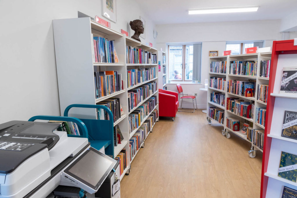 Fiction collection at Street Library with browsing shelves, comfortable seating by a window, display shelving and printing facilities nearby.