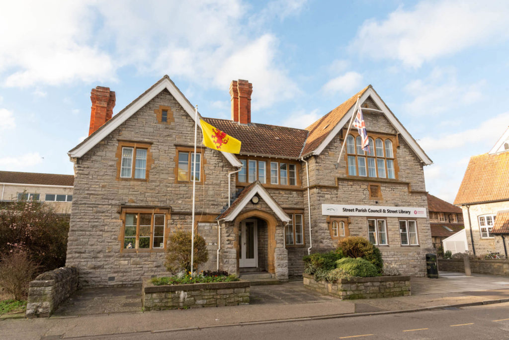 Exterior of Street Library and Street Parish Council, a historic stone building with a central entrance, large windows, landscaped frontage and library signage facing the street.
