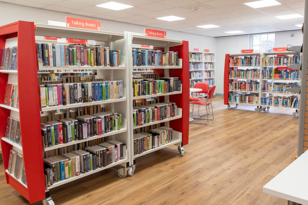 Talking books and fiction collections at Shepton Mallet Library with clearly labelled shelving, comfortable seating and wide aisles for browsing and borrowing.