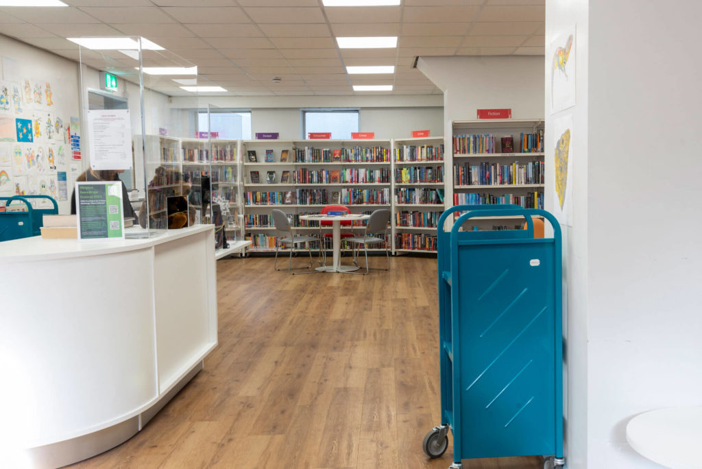 Main library area at Shepton Mallet Library with fiction collections, customer service desk, browsing shelves and seating for reading, study and community use.