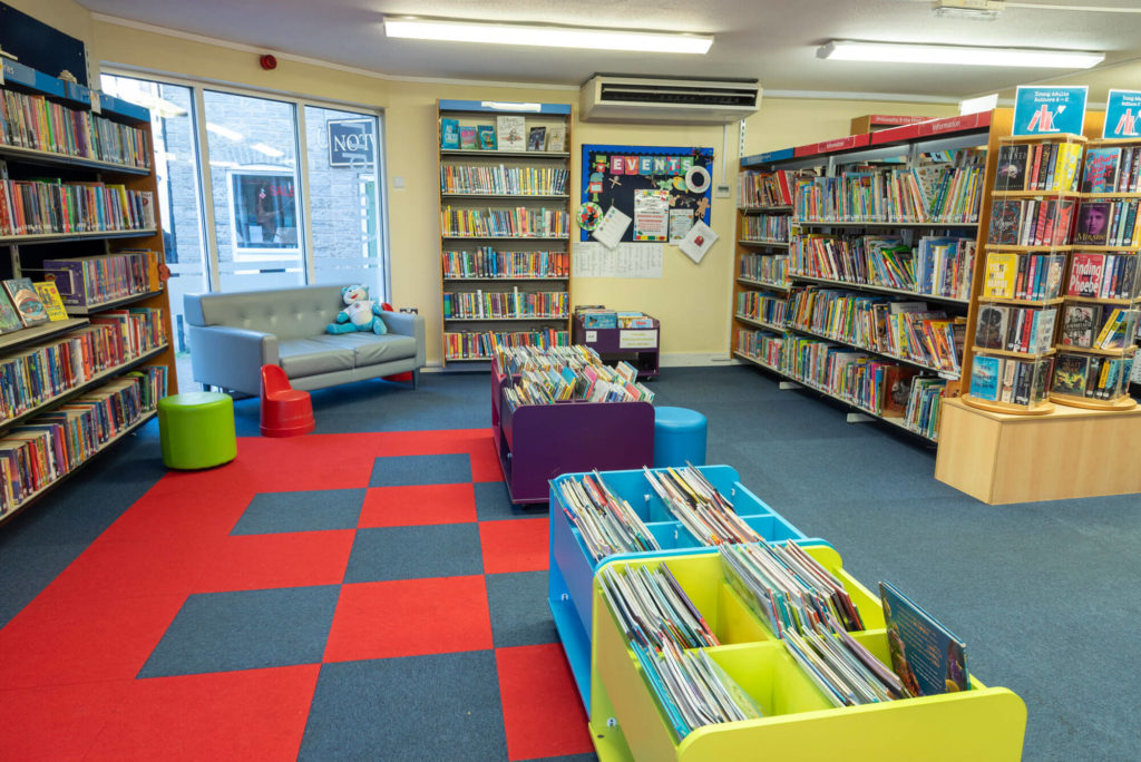 Children's and young adult area at Wells Library with colourful low-level book displays, seating, extensive shelves of children's books and space for reading and library activities.