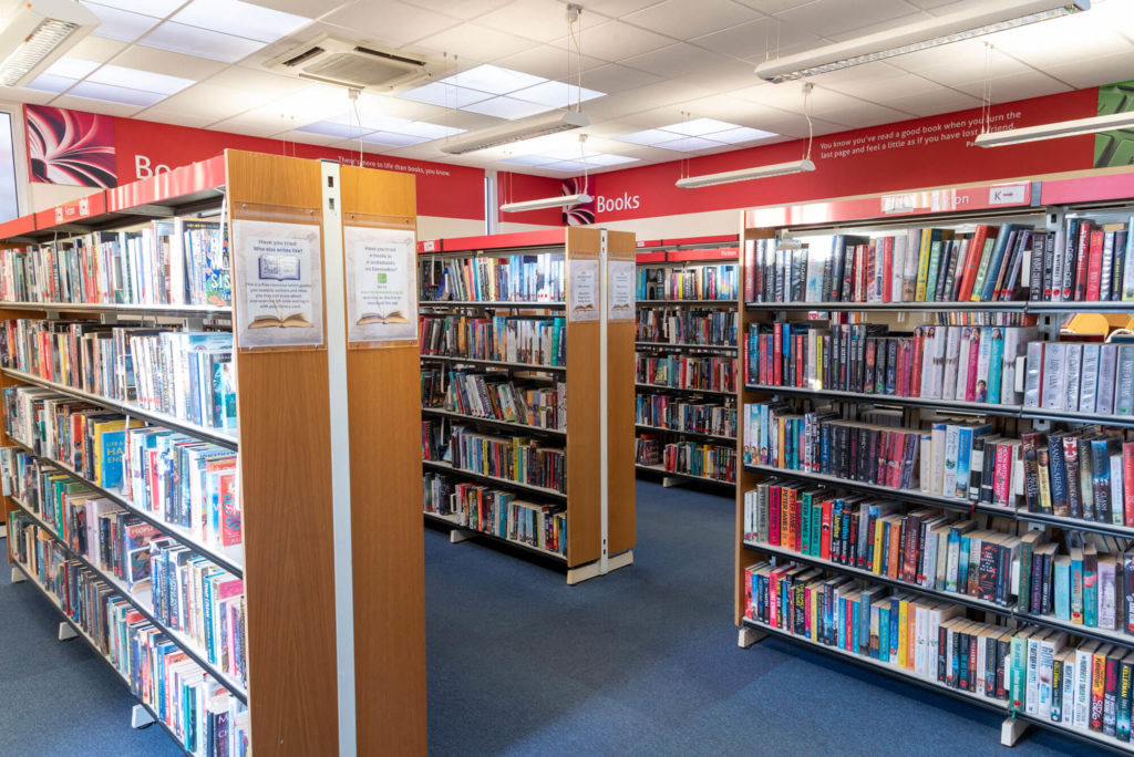 Adult fiction area at Wells Library with extensive rows of bookshelves, clearly labelled collections and wide aisles for browsing and borrowing.