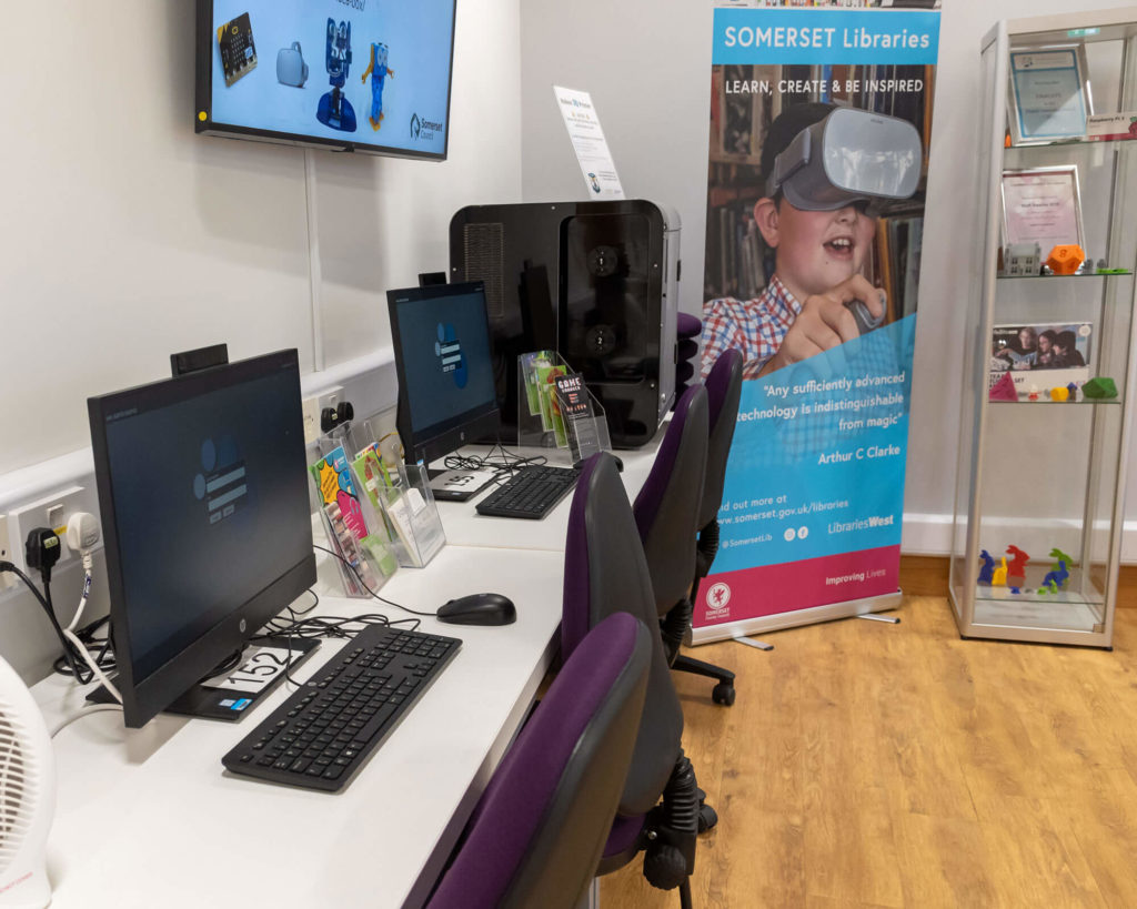 Digital technology area at Taunton Library with public computer workstations, a 3D printer, technology displays and information about the library's creative digital services.