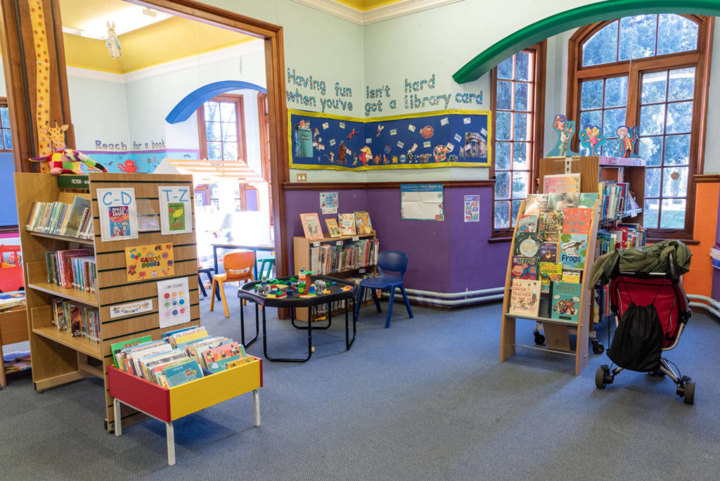 Children’s library area with colourful book displays, seating, activity table and shelves of children’s books.