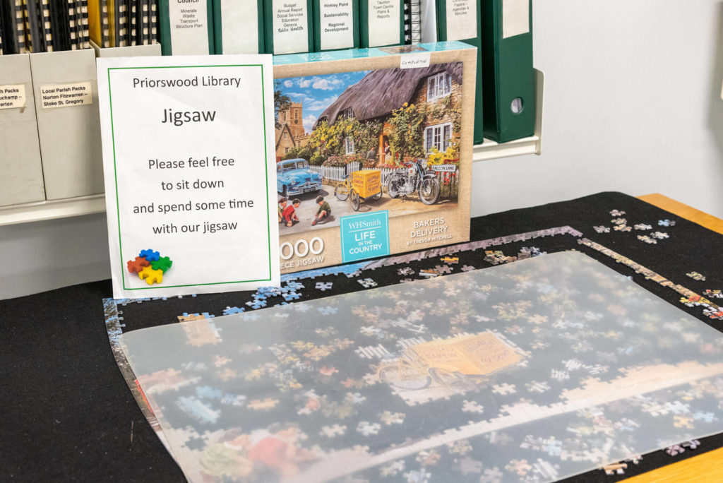 Community jigsaw puzzle at Priorswood Library with a partially completed countryside scene, puzzle pieces in progress and an invitation for visitors to take part.