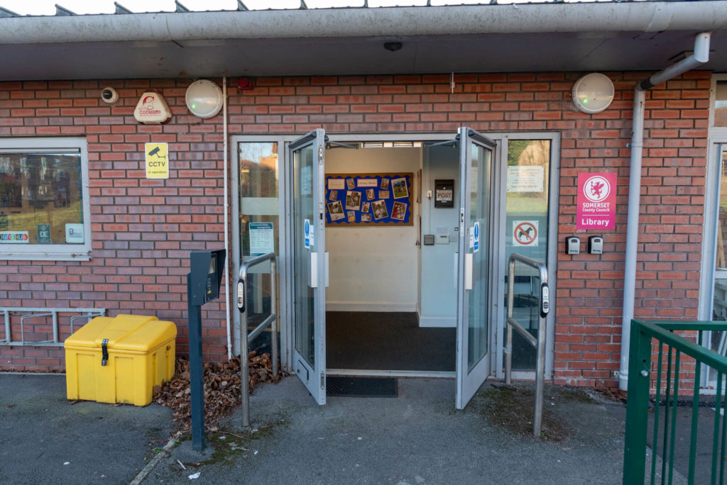 Exterior of Priorswood Library showing the main entrance with accessible automatic doors, handrails, library signage and a red-brick building frontage.