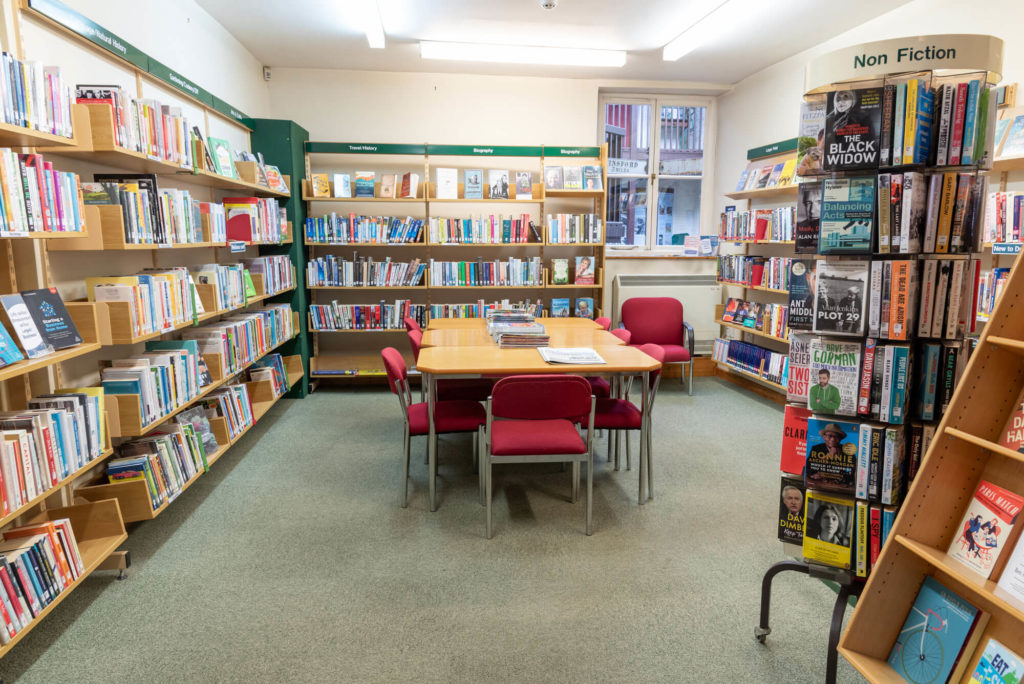 Main reading area at Dulverton Library with non-fiction and local interest book shelves, study tables and seating for browsing and reading.