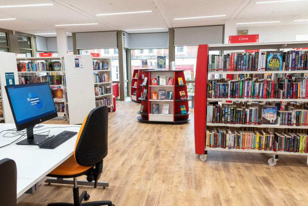Adult lending area at Minehead Library with fiction and crime collections, public computer workstation, featured book displays and wide aisles for browsing.