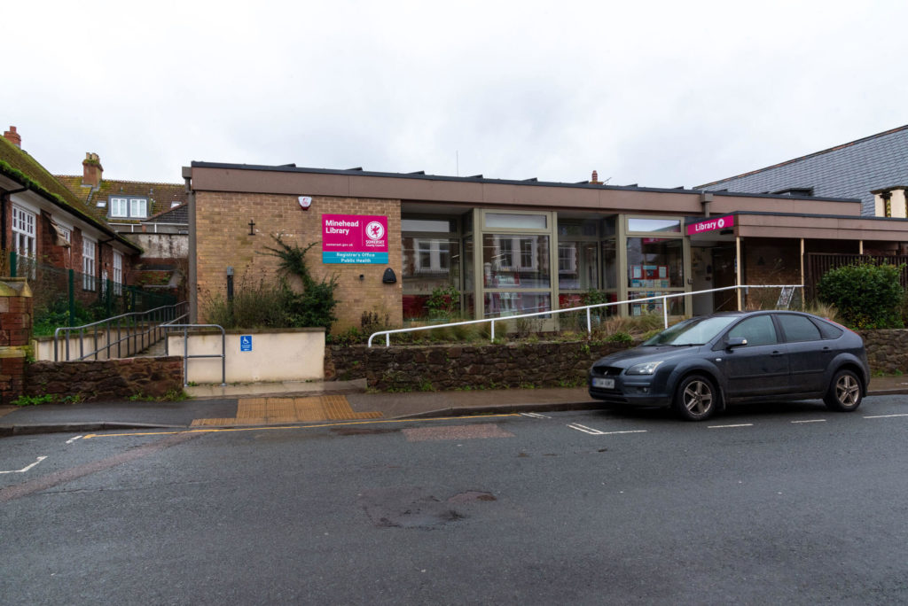 Exterior of Minehead Library showing the modern library building, accessible ramp, large front windows and main entrance facing the street.