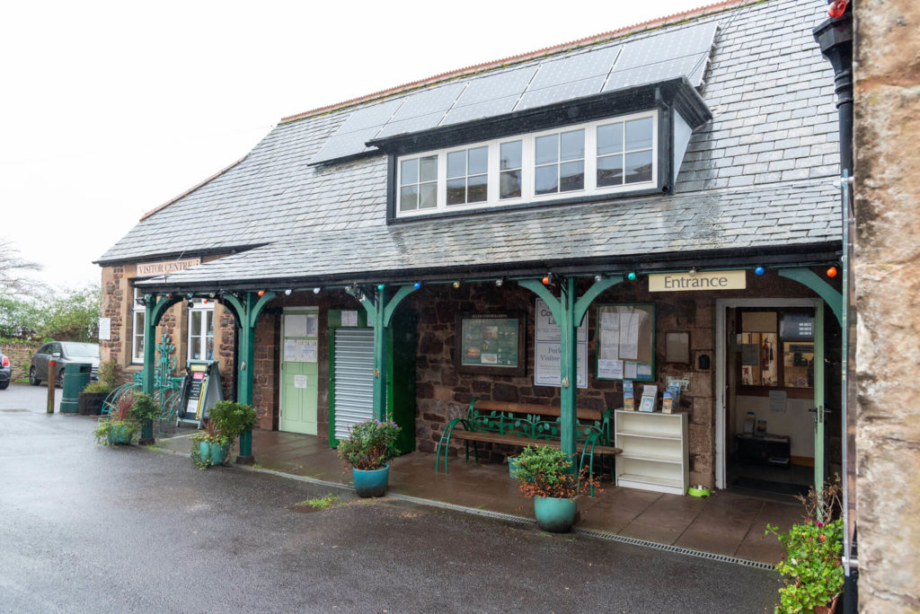 Exterior of Porlock Library and Visitor Centre, showing the shared entrance, covered walkway, seating, information displays and a stone-built building