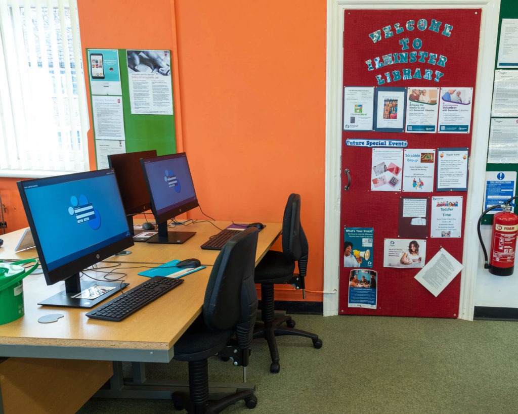 Public access computer area at Ilminster Library with desktop workstations, internet access facilities and information boards promoting library services and events.