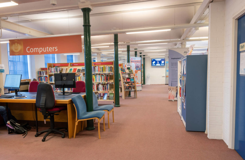 Public computer area at Chard Library with desktop workstations, bookshelves and clearly marked Computers section.