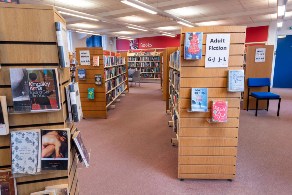 Adult fiction section at Chard Library with rows of bookshelves, featured book displays and clearly labelled browsing aisles.