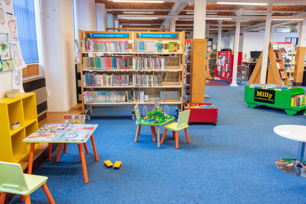 Children's area at Chard Library with low bookshelves, colourful seating, activity tables and books for younger readers.