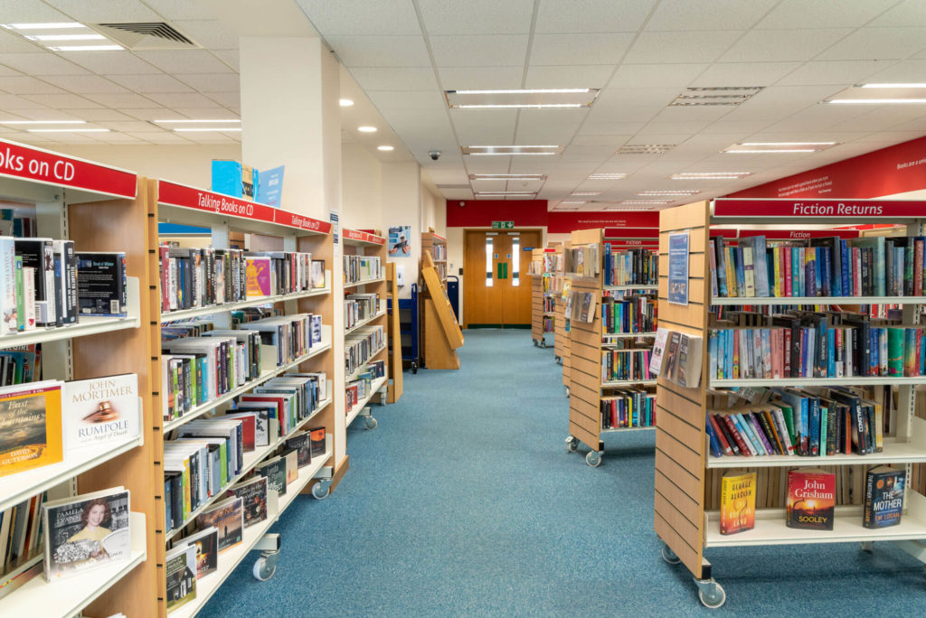 Adult lending area at Yeovil Library with fiction books, talking books on CD and clearly labelled shelving arranged in wide aisles for browsing and borrowing.