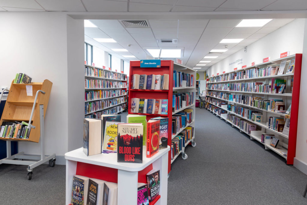 Main lending area at Wellington Library with extensive fiction and non-fiction collections, a new books display, long rows of shelving and wide aisles for browsing and borrowing.