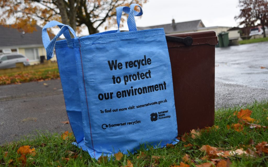 A blue recycling bag and a brown food waste bin on a driveway