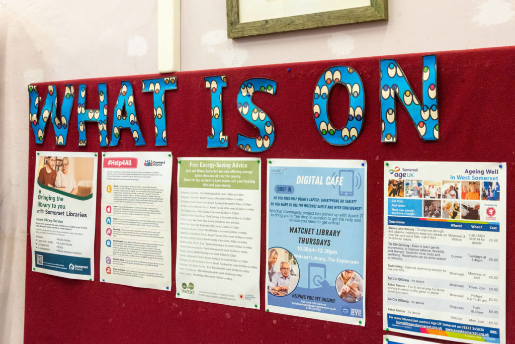 Community information noticeboard at Watchet Library displaying local service leaflets, digital support sessions, energy-saving advice and library information for residents.