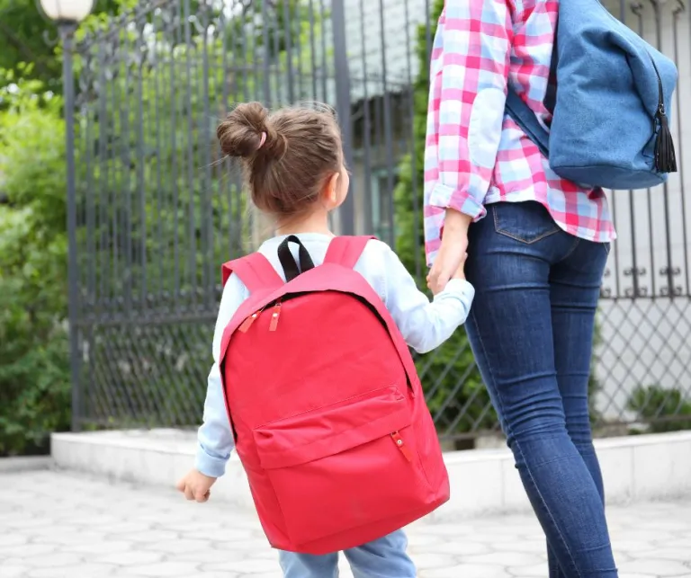 A woman and a child walking with backpacks on holding hands