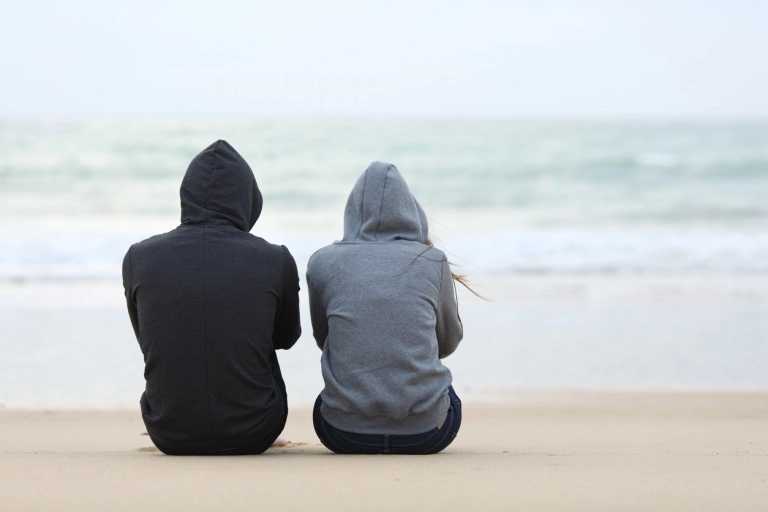 Two teenagers sitting on a beach looking at the water