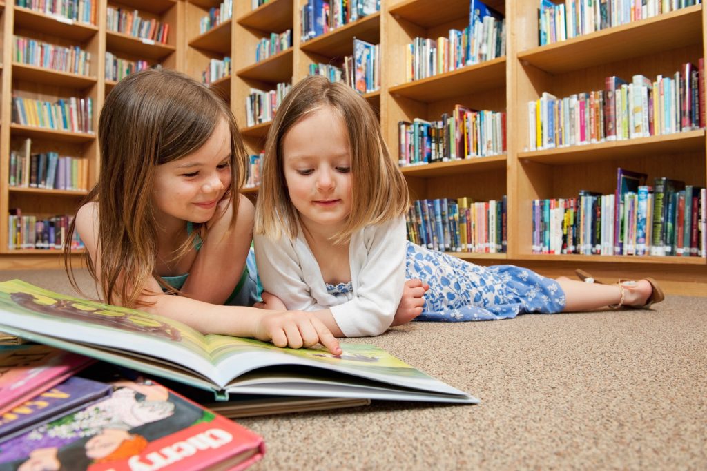 picture of two young girls lying on floor reading