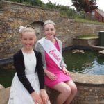 Photo of two girls sitting next to water fountain, one is wearing a carnival winner sash