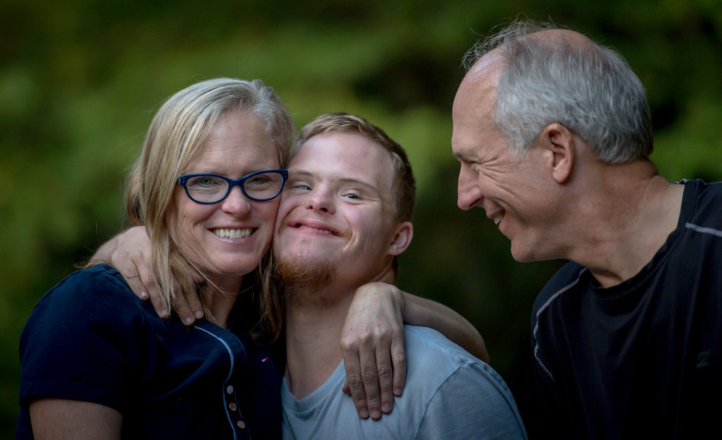 A man and a woman hugging a young boy with downs syndrome