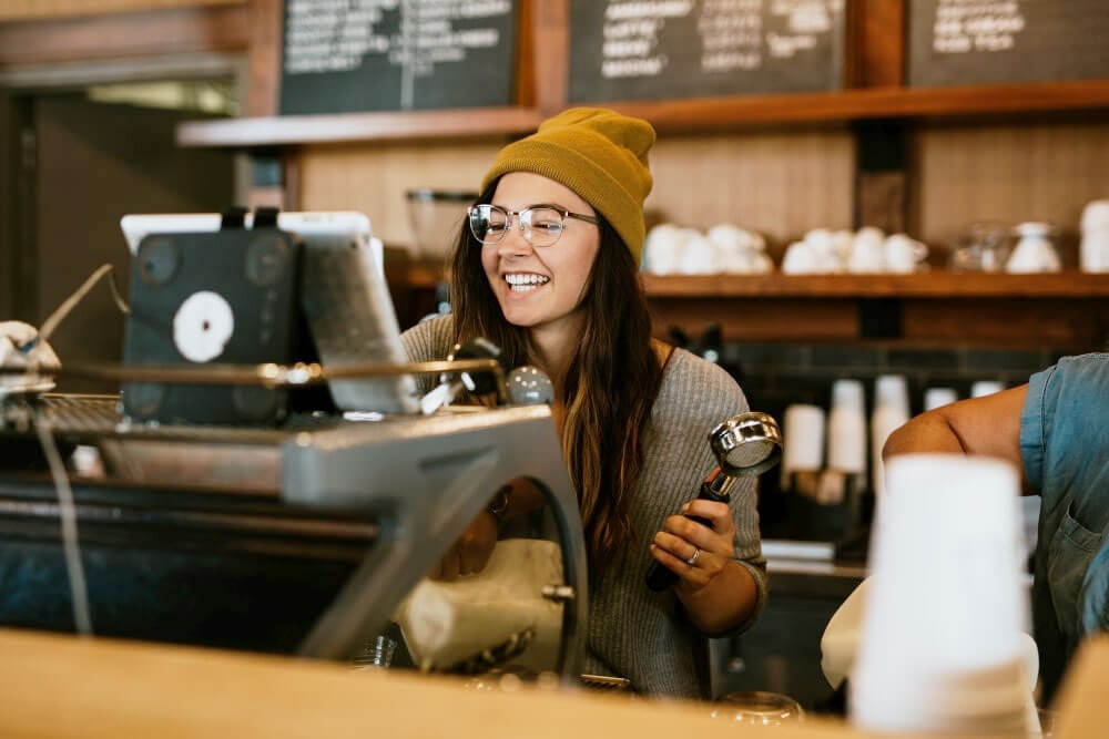A woman in a coffee shop smiling while making coffee.