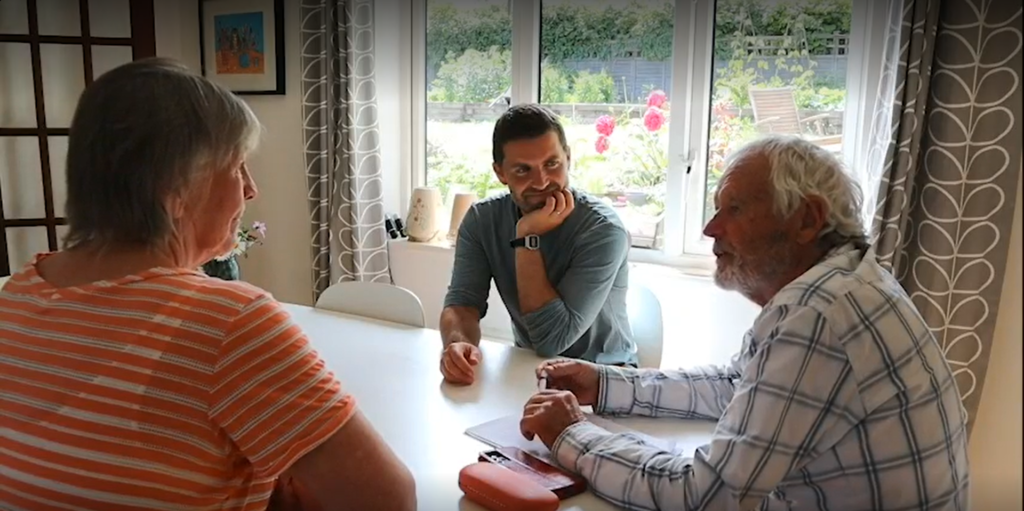 Image of three people sat around a table. A man is talking while a man and a woman listen.