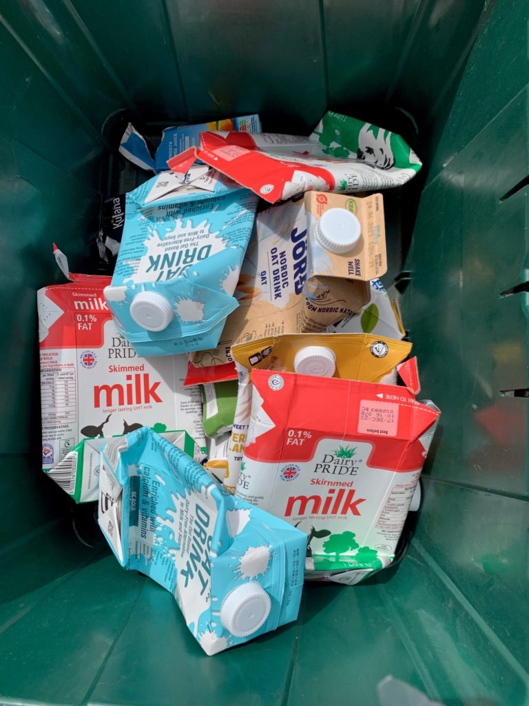 A green kerbside recycling box full of cartons for recycling