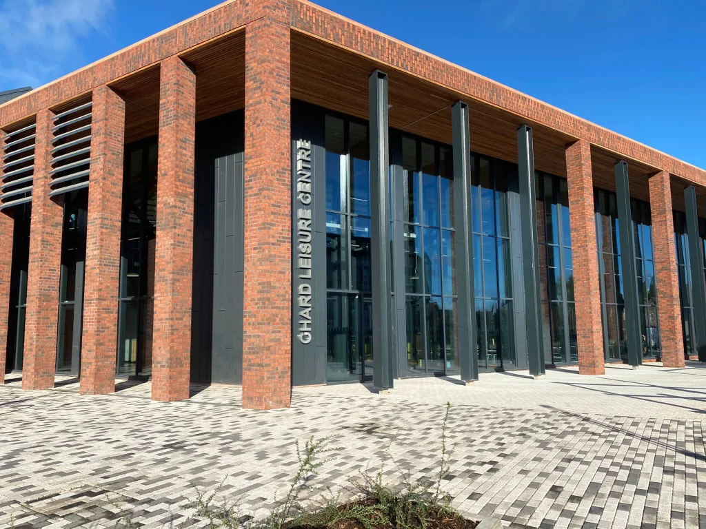 The outside of Chard Leisure Centre on a sunny day. It is a large red brick building with floor to ceiling windows.