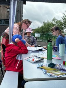 Students doing arts and crafts on outside table with adult helping