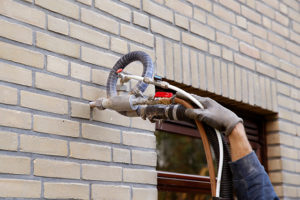 A worker wearing gloves injecting cavity wall insulation on an exterior wall