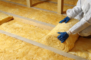 A worker in full protective gear installing loft insulation rolls