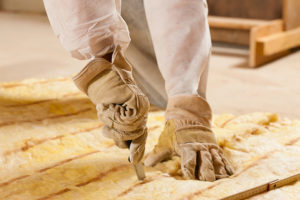 A worker wearing full protective gear installing under-floor insulation