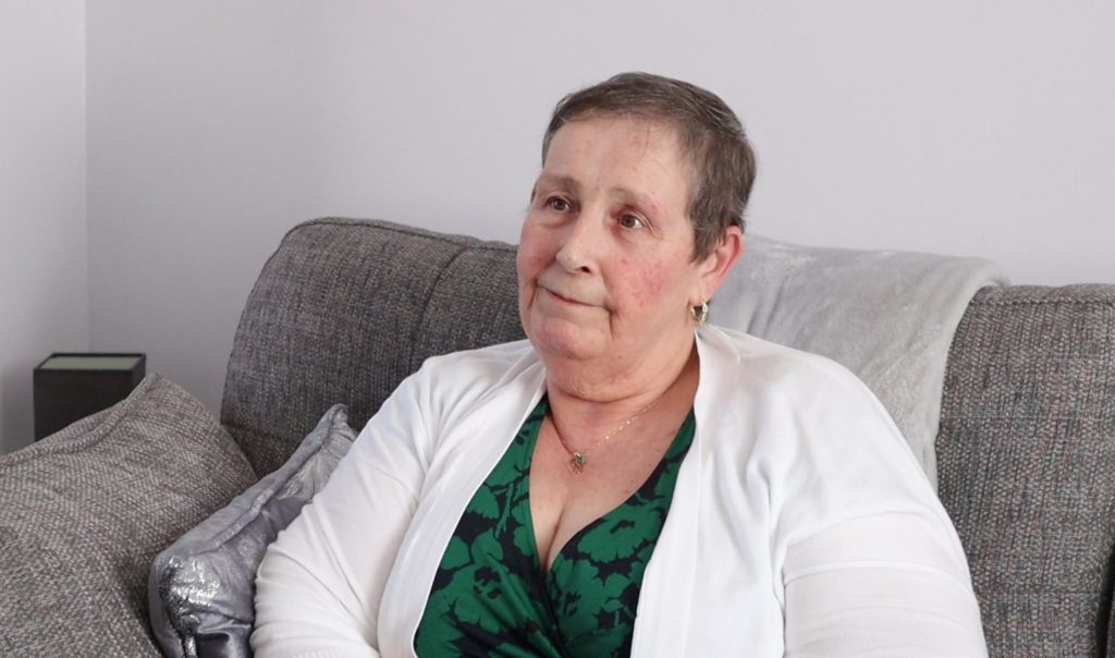 Jayne, a Somerset Council foster carer, sitting on her sofa smiling.