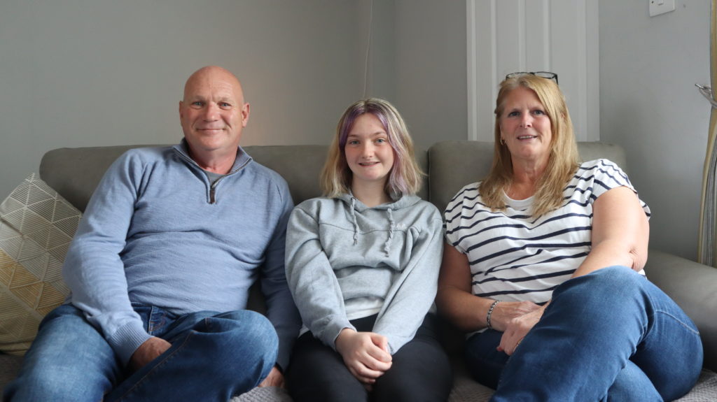 Stepping Stones carers Andy and Suzanne sat on a sofa with their Stepping Stones young person Jazz