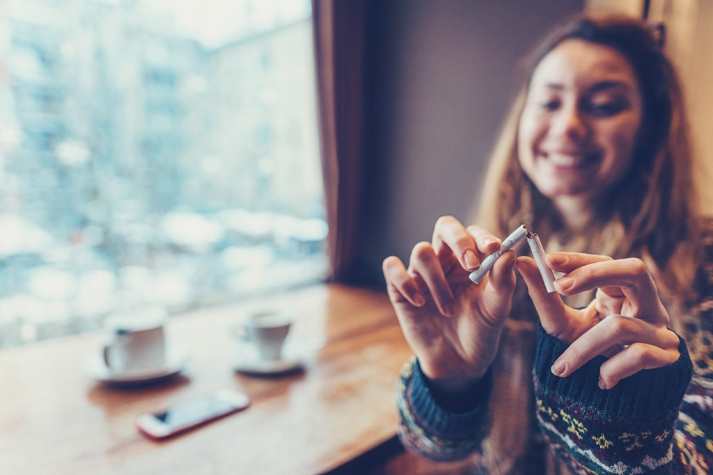 Quit smoking concept with young smiling woman sitting at the café and tearing her cigarette