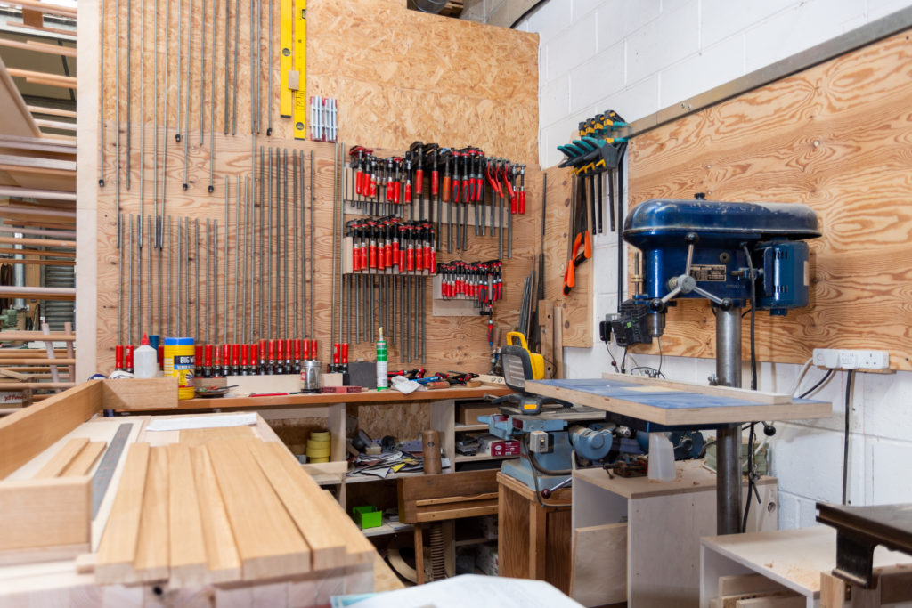 An inside view of the workshop. There's a range of tools on the walls and a pillar drill.