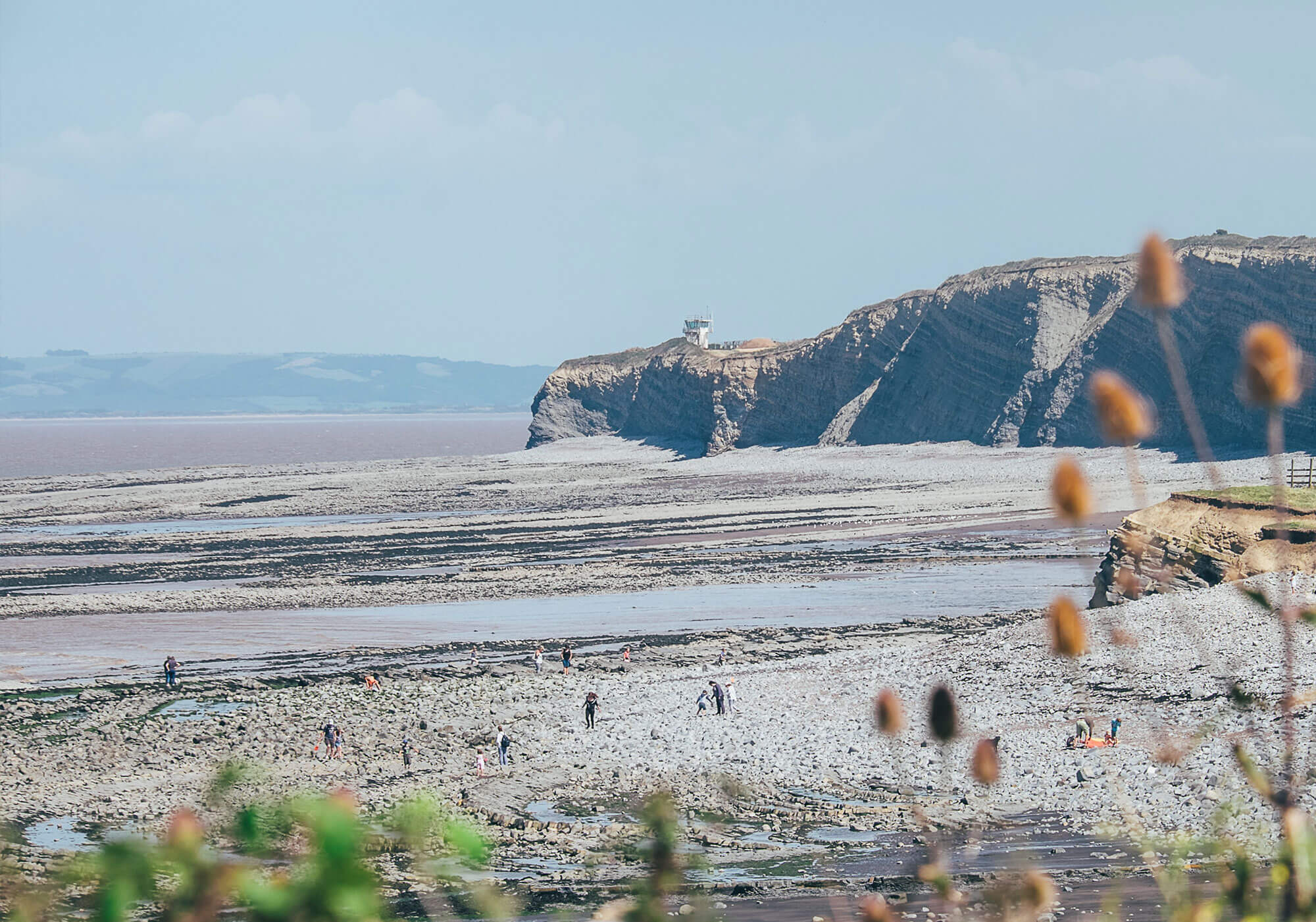 Looking out across a large beach, with a cliff in the distance. It's a hazy summer day.