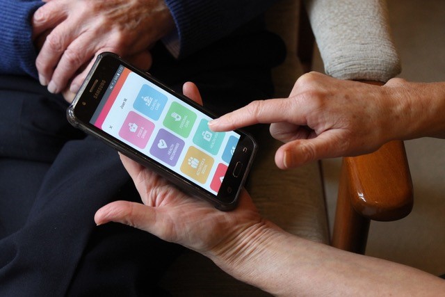 Finger pointing at a mobile screen which demonstrates the digital care record system.