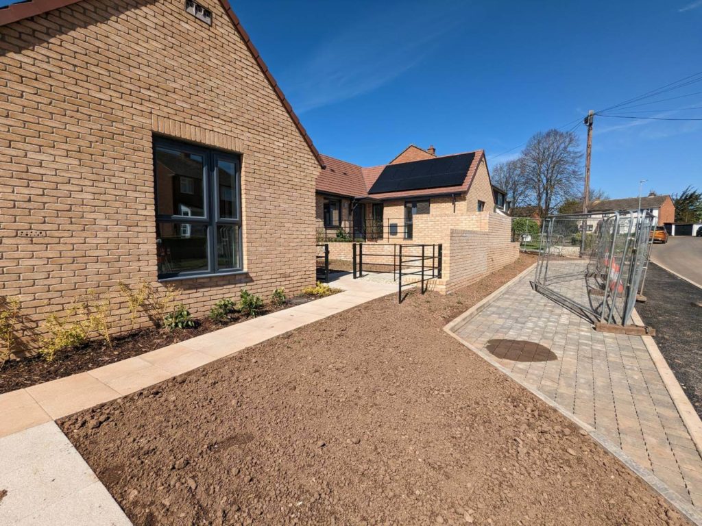 The image shows a wheelchair-adapted homes with a pitched roof and solar panels. In front of the house, there’s a small garden.