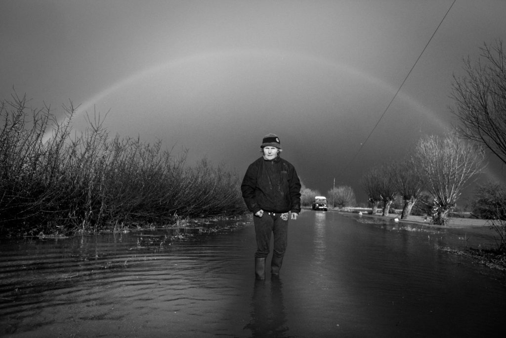 Person stood in the middle of flooded road with a rainbow above them.