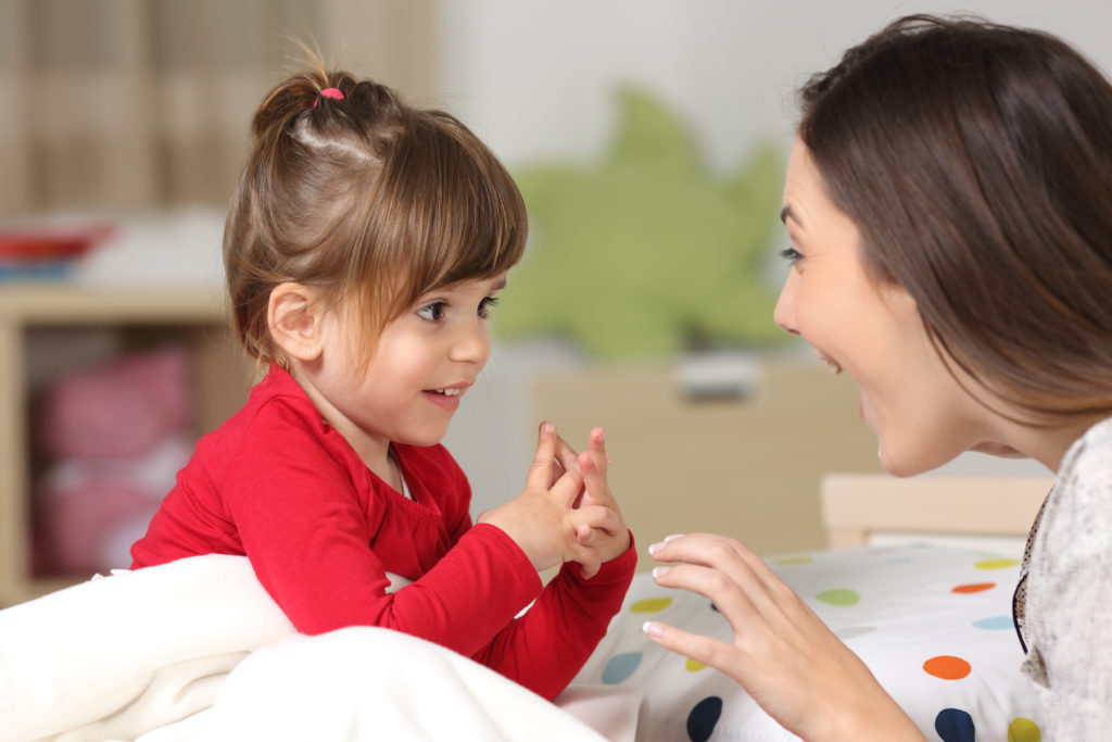 Mother and toddler wearing red shirt playing together on a bed in the bedroom at home