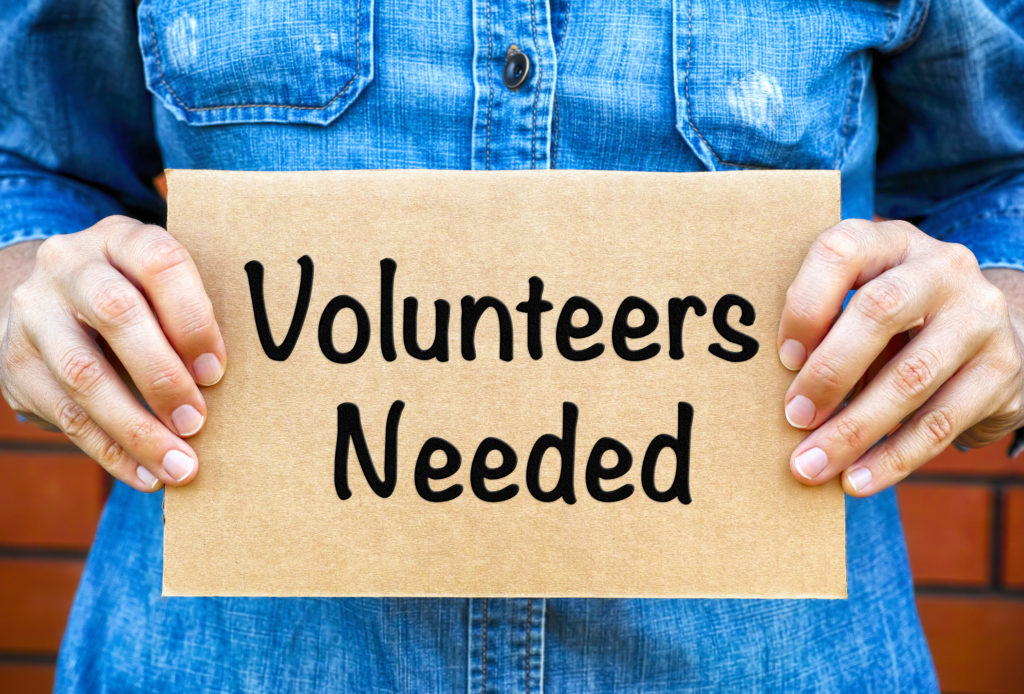 Woman hands holding piece of cardboard with words Volunteers Needed