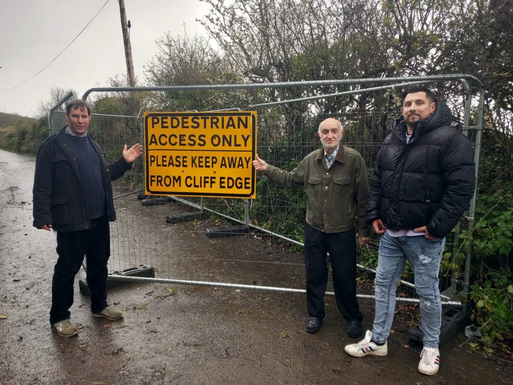 Photo of people pointing to a yellow pedestrian access only sign on a metal fence