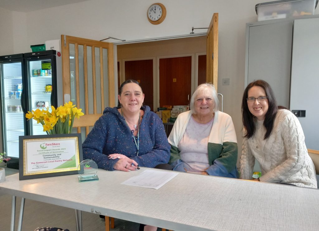 Three people sat a table smiling with a certificate and daffodils.