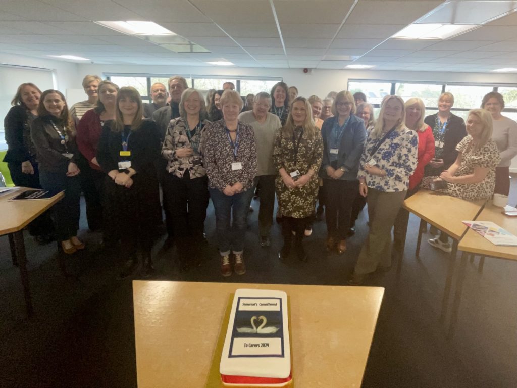 A group of people stand in front of a table which has a cake on it.